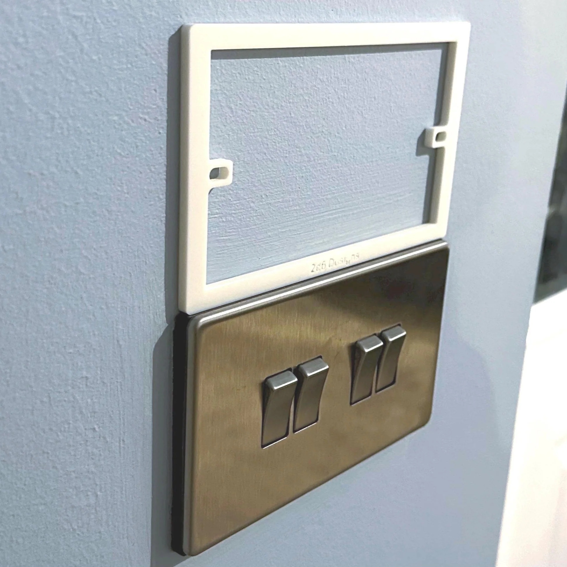 A white socket spacer fitted behind a brushed-brass double light switch, holding the faceplate away from the wall